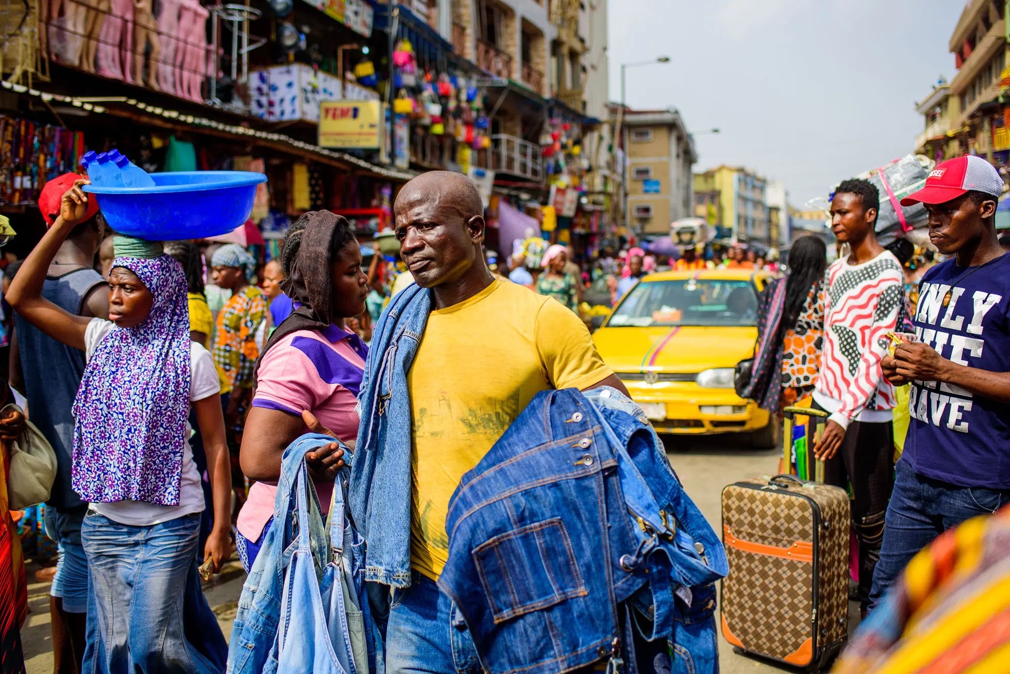 A market stall crowded with goods and shoppers, umbrellas overhead.