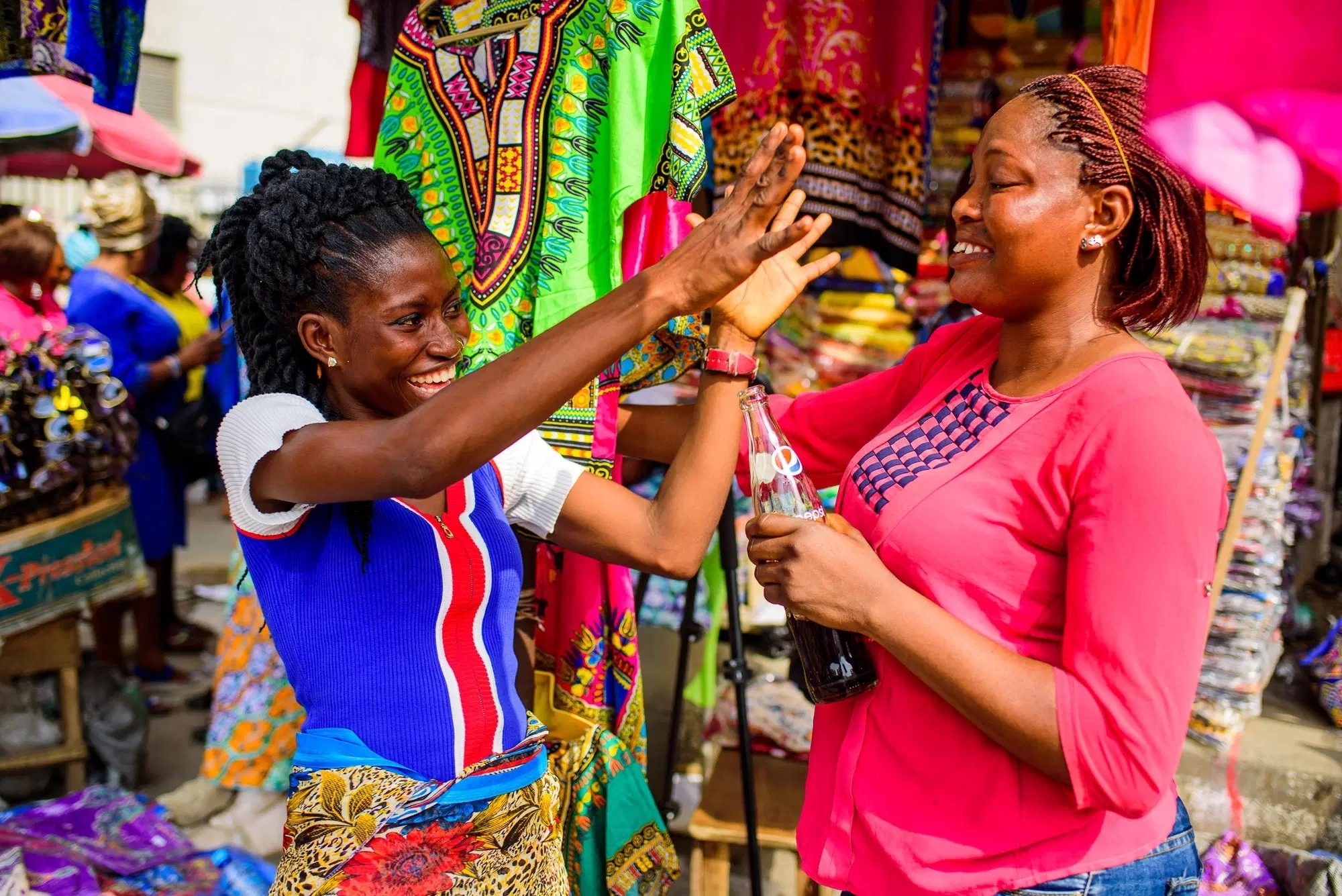 Two women high-fiving between fabric stalls.
